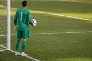 Fußballtorwart steht mit dem Ball in der Hand vor dem eigenen Tor und wartet auf die Spielfortsetzung.