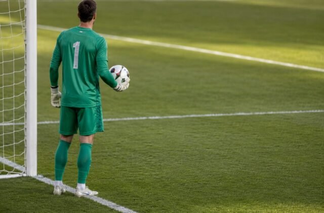 Fußballtorwart steht mit dem Ball in der Hand vor dem eigenen Tor und wartet auf die Spielfortsetzung.
