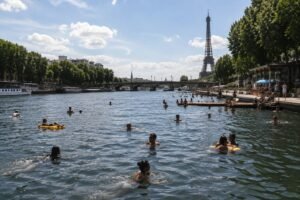 Menschen schwimmen an einem sonnigen Sommertag in der Seine in Paris, im Hintergrund ist der Eiffelturm zu sehen.