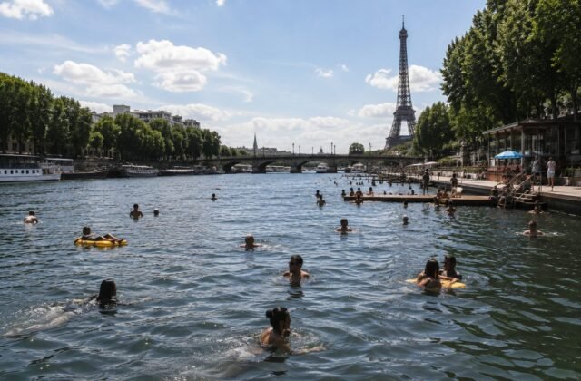 Menschen schwimmen an einem sonnigen Sommertag in der Seine in Paris, im Hintergrund ist der Eiffelturm zu sehen.
