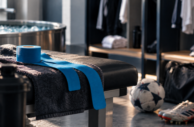 Blaues Kinesio-Tape auf einer Behandlungsliege neben Fußballschuhen, Ball und Eisbad in einem professionellen Recovery-Bereich.